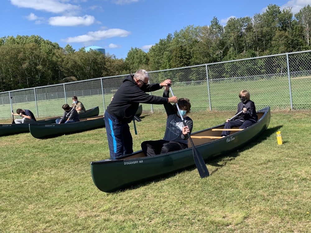 Students practicing canoeing outdoors on the ground.