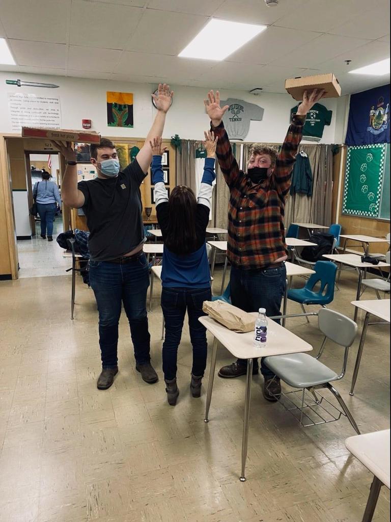 Students holding up pizza in a classroom.